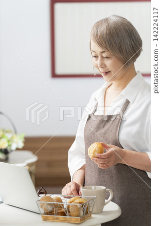 一位老婦人在客廳窗邊使用筆記型電腦。 一位老婦人在客廳窗邊使用筆記型電腦。 142224117