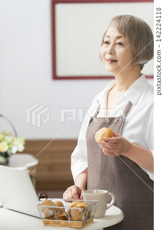 一位老婦人在客廳窗邊使用筆記型電腦。 一位老婦人在客廳窗邊使用筆記型電腦。 142224118