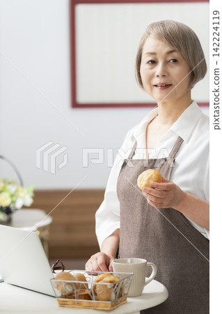 一位老婦人在客廳窗邊使用筆記型電腦。 一位老婦人在客廳窗邊使用筆記型電腦。 142224119