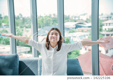 Relax woman yawning sitting on cozy sofa in apartment. Asian woman relax stretching arm laziness comfortable in living room. Happiness girl lifestyles sitting at home living room. Stretching arm relax Relax woman yawning sitting on cozy sofa in apartment. Asian woman relax stretching arm laziness comfortable in living room. Happiness girl lifestyles sitting at home living room. Stretching arm relax 142225106