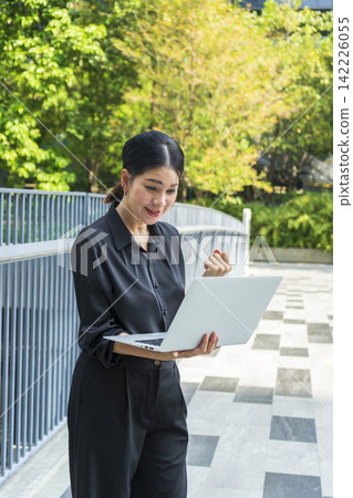 Business woman with computer laptop working outside in the park. Female professional businesswoman working outdoors. Business woman with computer laptop working outside in the park. Female professional businesswoman working outdoors. 142226055