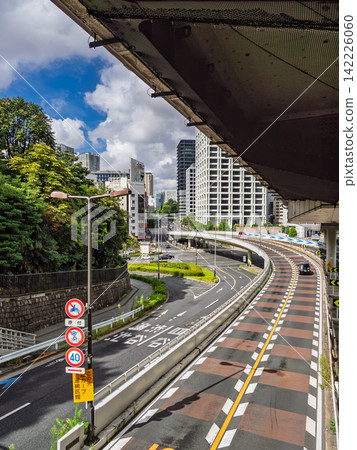 一條蜿蜒的道路從高架公路下方穿過,遠處是東京的城市景觀。 一條蜿蜒的道路從高架公路下方穿過,遠處是東京的城市景觀。 142226060