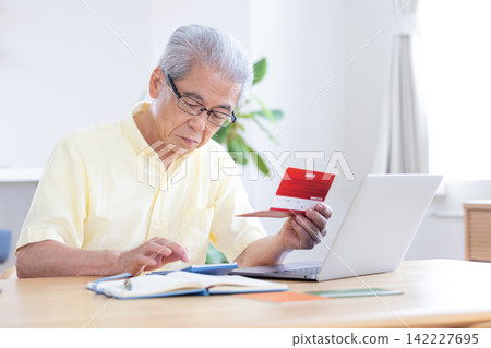 一位老人在客廳看著他的銀行存摺。 一位老人在客廳看著他的銀行存摺。 142227695