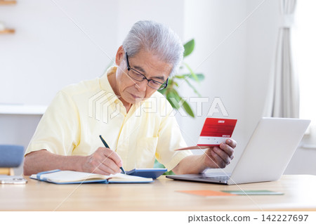 A senior man looking at his bankbook in the living room. A senior man looking at his bankbook in the living room. 142227697
