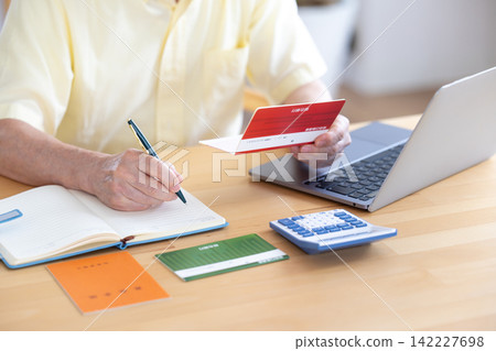A senior man looking at his bankbook in the living room. A senior man looking at his bankbook in the living room. 142227698