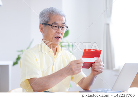 一位老人在客廳看著他的銀行存摺。 一位老人在客廳看著他的銀行存摺。 142227700