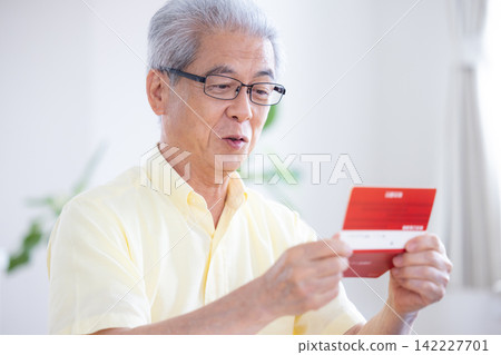 一位老人在客廳看著他的銀行存摺。 一位老人在客廳看著他的銀行存摺。 142227701
