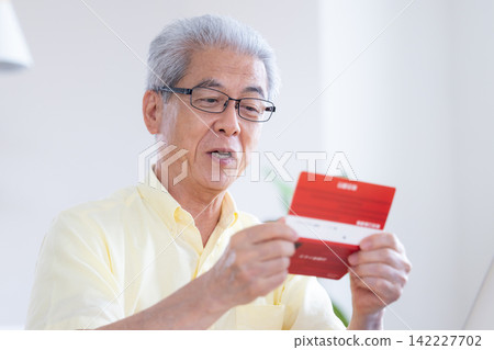 一位老人在客廳看著他的銀行存摺。 一位老人在客廳看著他的銀行存摺。 142227702