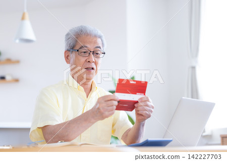 A senior man looking at his bankbook in the living room. A senior man looking at his bankbook in the living room. 142227703