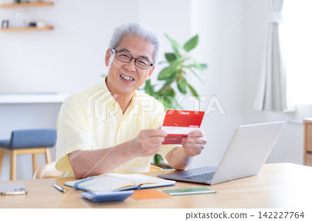 A senior man looking at his bankbook in the living room. A senior man looking at his bankbook in the living room. 142227764