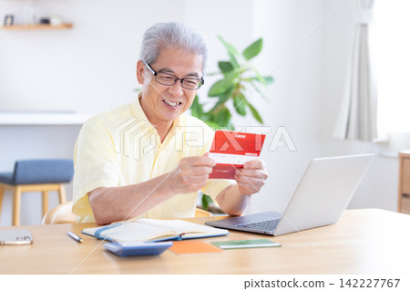 A senior man looking at his bankbook in the living room. A senior man looking at his bankbook in the living room. 142227767