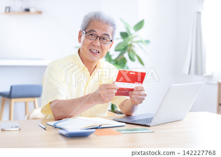 A senior man looking at his bankbook in the living room. A senior man looking at his bankbook in the living room. 142227768