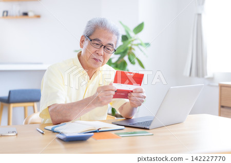 A senior man looking at his bankbook in the living room. 142227770