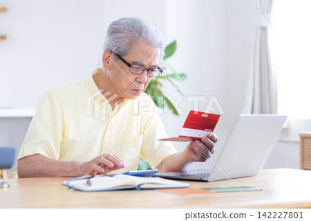 A senior man looking at his bankbook in the living room. A senior man looking at his bankbook in the living room. 142227801