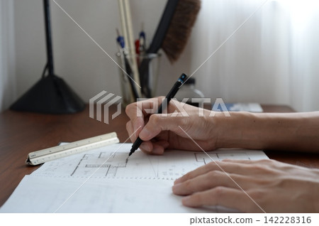 一名男子正在素描本上繪製建築設計圖。 一名男子正在素描本上繪製建築設計圖。 142228316