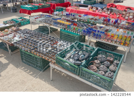 古董市集攤位:舊鐵壺、古董工具和色彩鮮豔的玻璃器皿整齊地擺放在容器中。 古董市集攤位:舊鐵壺、古董工具和色彩鮮豔的玻璃器皿整齊地擺放在容器中。 142228544