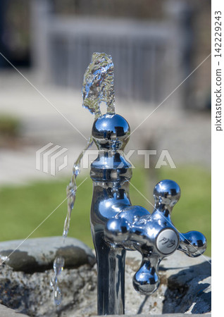 A close-up of water flowing from a drinking fountain in a park, showing people rehydrating. A close-up of water flowing from a drinking fountain in a park, showing people rehydrating. 142229243