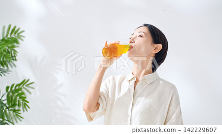 A woman drinking bottled tea. Hydration, oolong tea, green tea, black tea, barley tea, hydration, drinks, juice A woman drinking bottled tea. Hydration, oolong tea, green tea, black tea, barley tea, hydration, drinks, juice 142229607