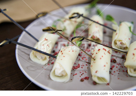 Cheese Roll Appetizers Skewered And Arranged On Ceramic Plate On Wooden Table With Crushed Red Cheese Roll Appetizers Skewered And Arranged On Ceramic Plate On Wooden Table With Crushed Red 142229703