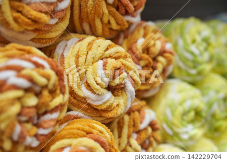 Yellow And White Chenille Yarn Balls Stacked On Display In Close-Up Showing Plush Twisted Texture Yellow And White Chenille Yarn Balls Stacked On Display In Close-Up Showing Plush Twisted Texture 142229704