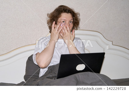 Woman Massaging Eyes In Front Of Open Laptop While Sitting In Bed, Expressing Eye Strain Woman Massaging Eyes In Front Of Open Laptop While Sitting In Bed, Expressing Eye Strain 142229728