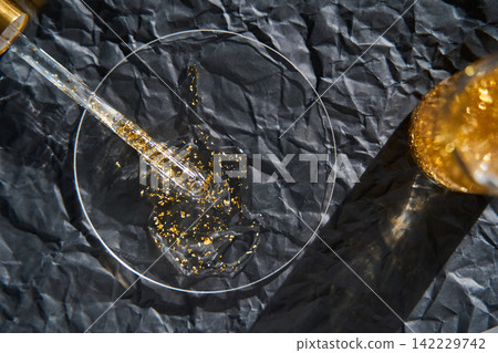 Viscous Clear Gel With Suspended Gold Flakes Applied With Pipette Into Glass Dish On Crumpled Dark Viscous Clear Gel With Suspended Gold Flakes Applied With Pipette Into Glass Dish On Crumpled Dark 142229742
