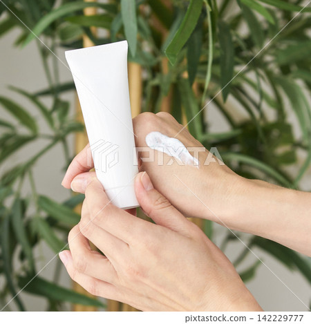 Hands Applying Cream From Tube On Skin With Plant Background Illustrating Natural Beauty Hands Applying Cream From Tube On Skin With Plant Background Illustrating Natural Beauty 142229777