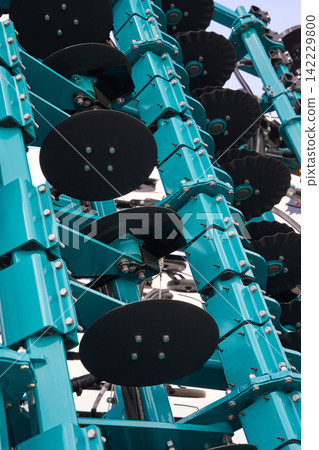 Teal Agricultural Harrow Assembly Mounted With Black Rotating Discs On Metal Frame Against Bright Teal Agricultural Harrow Assembly Mounted With Black Rotating Discs On Metal Frame Against Bright 142229800