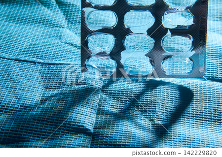Blister Pack With Multiple Emptied Compartments Hanging Above Textured Blue Drape Producing Strong Blister Pack With Multiple Emptied Compartments Hanging Above Textured Blue Drape Producing Strong 142229820