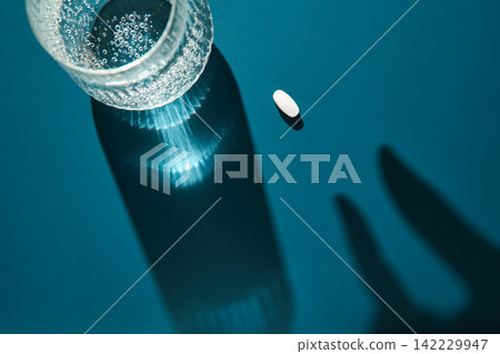 Glass Bottle Top With Effervescent Water And Lone White Tablet With Dual Hand Shadows On Blue Glass Bottle Top With Effervescent Water And Lone White Tablet With Dual Hand Shadows On Blue 142229947