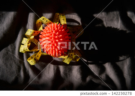 Spiky Orange Massage Ball Wrapped With Yellow Measuring Tape Resting On Dark Wrinkled Fabric 142230278