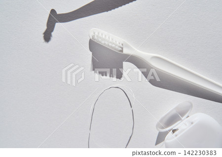 Toothbrush Placed Next To Dental Floss Container On White Textured Paper Surface With Distinct Soft Toothbrush Placed Next To Dental Floss Container On White Textured Paper Surface With Distinct Soft 142230383