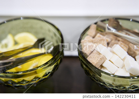 Two Green Cut Glass Bowls Containing Lemon Slices And Mixed Sugar Cubes With Metal Tongs Placed Two Green Cut Glass Bowls Containing Lemon Slices And Mixed Sugar Cubes With Metal Tongs Placed 142230411