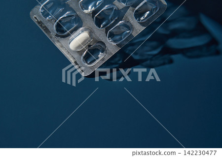 Single White Pill Remaining In Blister Pack Resting On Dark Blue Tabletop With Reflective Foil Single White Pill Remaining In Blister Pack Resting On Dark Blue Tabletop With Reflective Foil 142230477