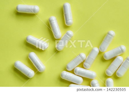 Closeup Of White Capsules Scattered On Yellow Background Removed From Blue Glass Bottle Studio 142230505