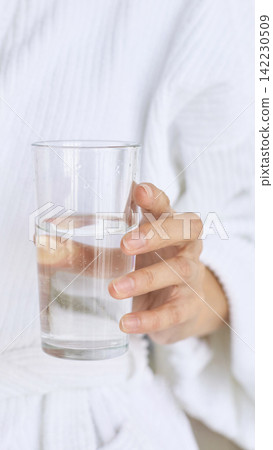 Hand Holding Glass Of Water Wearing White Robe Indoors Bathroom Or Bedroom Setting Closeup Showing Hand Holding Glass Of Water Wearing White Robe Indoors Bathroom Or Bedroom Setting Closeup Showing 142230509