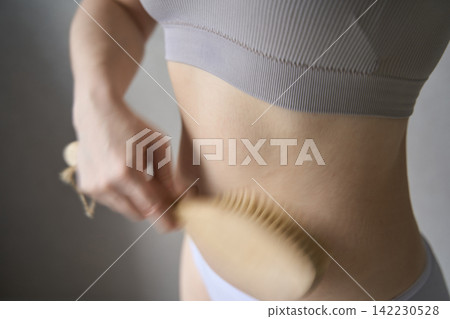 Young Woman Dry Brushing Waist And Abdomen In Soft Indoor Home Setting With Neutral Lighting Young Woman Dry Brushing Waist And Abdomen In Soft Indoor Home Setting With Neutral Lighting 142230528