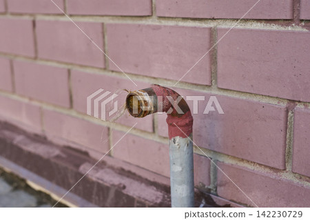 Exposed Water Pipe Elbow Protruding From Pink Brick Wall Outdoors Closeup Showing Rusted Fitting Exposed Water Pipe Elbow Protruding From Pink Brick Wall Outdoors Closeup Showing Rusted Fitting 142230729