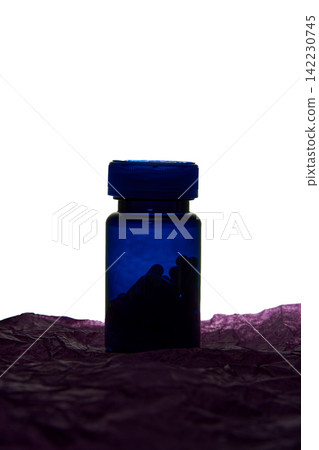 Blue Medicine Bottle Silhouette With Screw Cap Standing On Crumpled Purple Tissue Against White Blue Medicine Bottle Silhouette With Screw Cap Standing On Crumpled Purple Tissue Against White 142230745