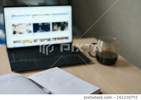 Open Notebook Pen And Coffee Mug In Front Of Laptop Displaying Blurred Website Thumbnails On Wooden Open Notebook Pen And Coffee Mug In Front Of Laptop Displaying Blurred Website Thumbnails On Wooden 142230755