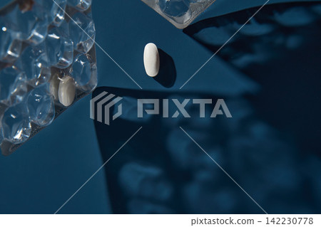 White Pill Resting Deep Blue Tabletop With Partially Empty Blister Pack Casting Textured Shadows White Pill Resting Deep Blue Tabletop With Partially Empty Blister Pack Casting Textured Shadows 142230778