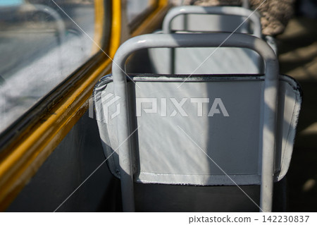 Closeup Of Bus Seat Back Facing Window Inside City Bus Showing Sunlit Vinyl Texture And Metal Closeup Of Bus Seat Back Facing Window Inside City Bus Showing Sunlit Vinyl Texture And Metal 142230837