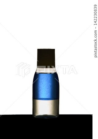 Glass Bottle Containing Blue Liquid Standing Upright On Black Surface Against White Background Glass Bottle Containing Blue Liquid Standing Upright On Black Surface Against White Background 142230839
