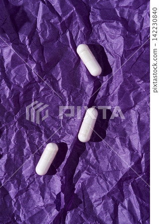 White Capsules Placed On Crumpled Purple Paper Background With Distinct Shadows And Textured Folds White Capsules Placed On Crumpled Purple Paper Background With Distinct Shadows And Textured Folds 142230840