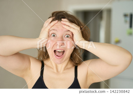 Woman Holding Forehead With Both Hands Displaying Astonished Open Mouth Expression In Small Home Woman Holding Forehead With Both Hands Displaying Astonished Open Mouth Expression In Small Home 142230842