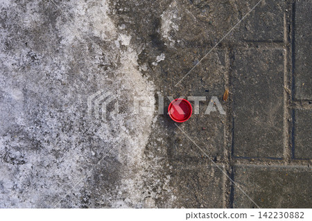 Red Bottle Cap Lying Beside Melting Snow On Patterned Concrete Sidewalk Tiles In Urban Winter Red Bottle Cap Lying Beside Melting Snow On Patterned Concrete Sidewalk Tiles In Urban Winter 142230882