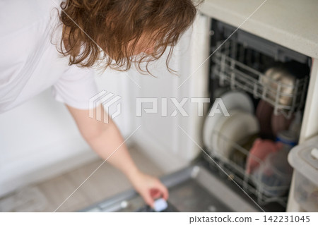 Woman Leaning Over Placing Dishwasher Detergent Tablet Into Dispenser On Open Dishwasher Door Woman Leaning Over Placing Dishwasher Detergent Tablet Into Dispenser On Open Dishwasher Door 142231045