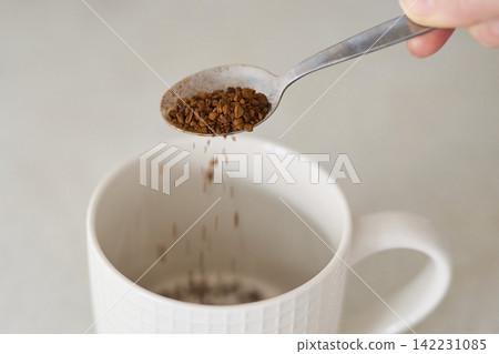 Instant Coffee Granules Falling From Metal Spoon Into White Textured Ceramic Mug On Light Instant Coffee Granules Falling From Metal Spoon Into White Textured Ceramic Mug On Light 142231085