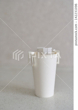 Tall Paper Cup With Drip Coffee Filter Attached To Rim Standing On Speckled Countertop Against Soft Tall Paper Cup With Drip Coffee Filter Attached To Rim Standing On Speckled Countertop Against Soft 142231096