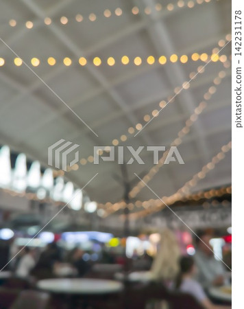 Overhead String Lights Glowing Above Blurred Cafe Seating With Vaulted Ceiling In Indoor Market 142231178